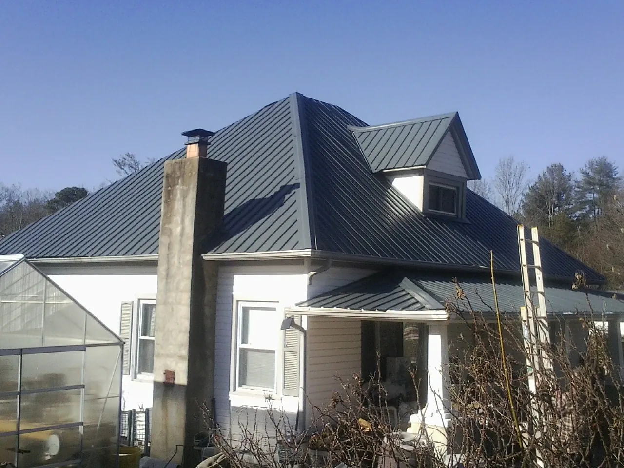 Dark blue standing seam metal roof on a white farmhouse with dormer — Slate & Tile Roof Repair by Roofing Brothers in Kiowa