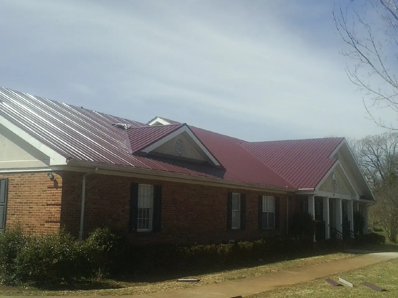 Red metal roof with gabled entries on a long brick building, from a Hail Damage Roof Repair job in Kiowa